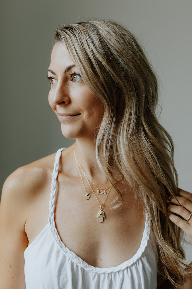 Woman wearing the Love Layering Necklace paired with the Hamsa + Evil Eye Necklaces
