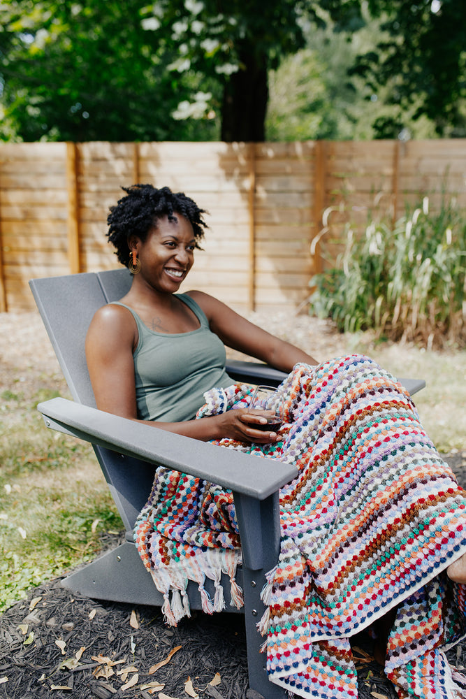 
            
                Load image into Gallery viewer, Woman sitting outside with the Rainbow Pom Pom Towel-Blanket
            
        